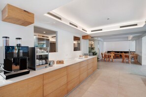 A modern kitchen with a coffee machine, cabinets, and a dining area with wooden chairs and a glass table.