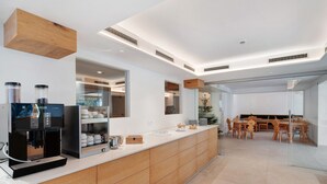 A modern kitchen with a coffee machine, cabinets, and a dining area with wooden chairs and a glass table. - Room with Mountain View and Wi-Fi (Vigo di Fassa)