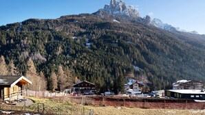 A mountain lodge with a wooden cabin, a larger building with a sloped roof, and a view of a rocky mountain peak. - Room with Mountain View and Wi-Fi (Vigo di Fassa)