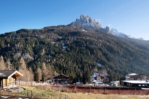 A mountain lodge with a wooden cabin, a larger building with a sloped roof, and a view of a rocky mountain peak.