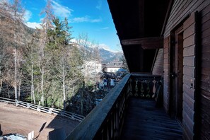 A wooden balcony with a view of a mountainous landscape and a village below.