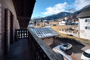 Un balcon en bois offrant une vue sur une montagne enneigée, une voiture garée et un bâtiment doté d’un toit en pente.