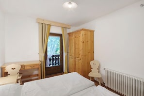 Une chambre avec un bureau en bois, une armoire, un radiateur et une fenêtre avec des rideaux.