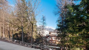 A mountainous landscape with a wooden bridge, trees, and buildings with a mountain in the background.