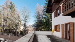 A building with wooden shutters, a balcony, and a view of trees and mountains.