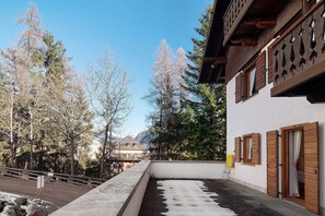 A building with wooden shutters, a balcony, and a view of trees and mountains.