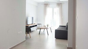 Uma sala de estar moderna com um sofá cinza, uma mesa de centro de madeira e uma TV sobre um móvel de madeira.