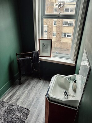 Un baño con ventana, un cuadro enmarcado, toallero y lavamanos.