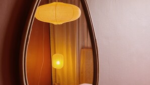 A mirror with an oval frame reflecting a room with a bed, a bedside table, and a hanging lamp. - Margate Manor (Margate)