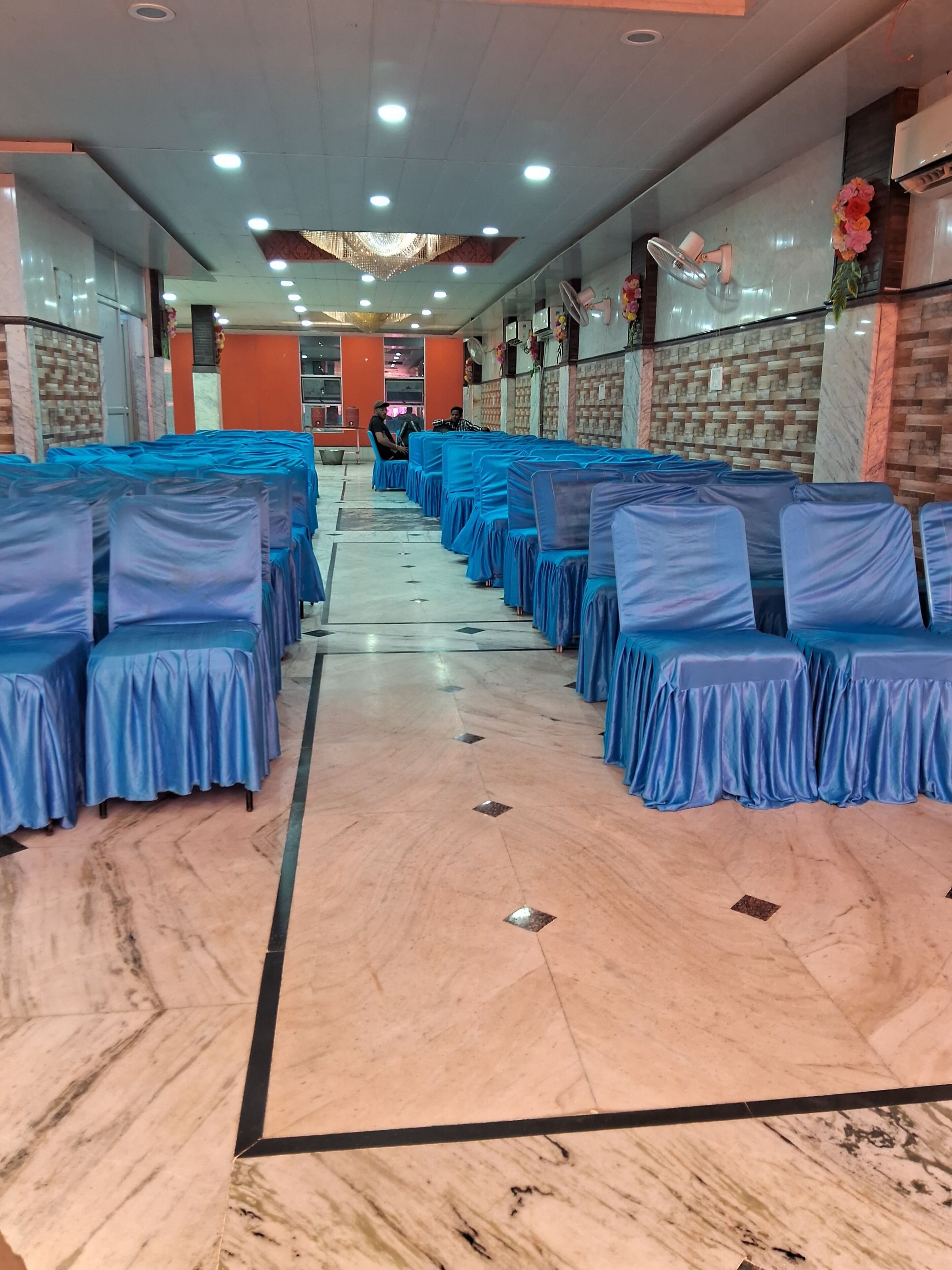 Un salón de banquetes con filas de mesas y sillas cubiertas de azul, suelo de mármol y una araña.