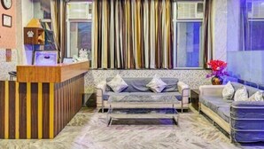 A hotel lobby with a reception desk, two sofas, patterned wallpaper, and a large window with curtains. - Hotel Shri Laxmi Palace (Kanpur)