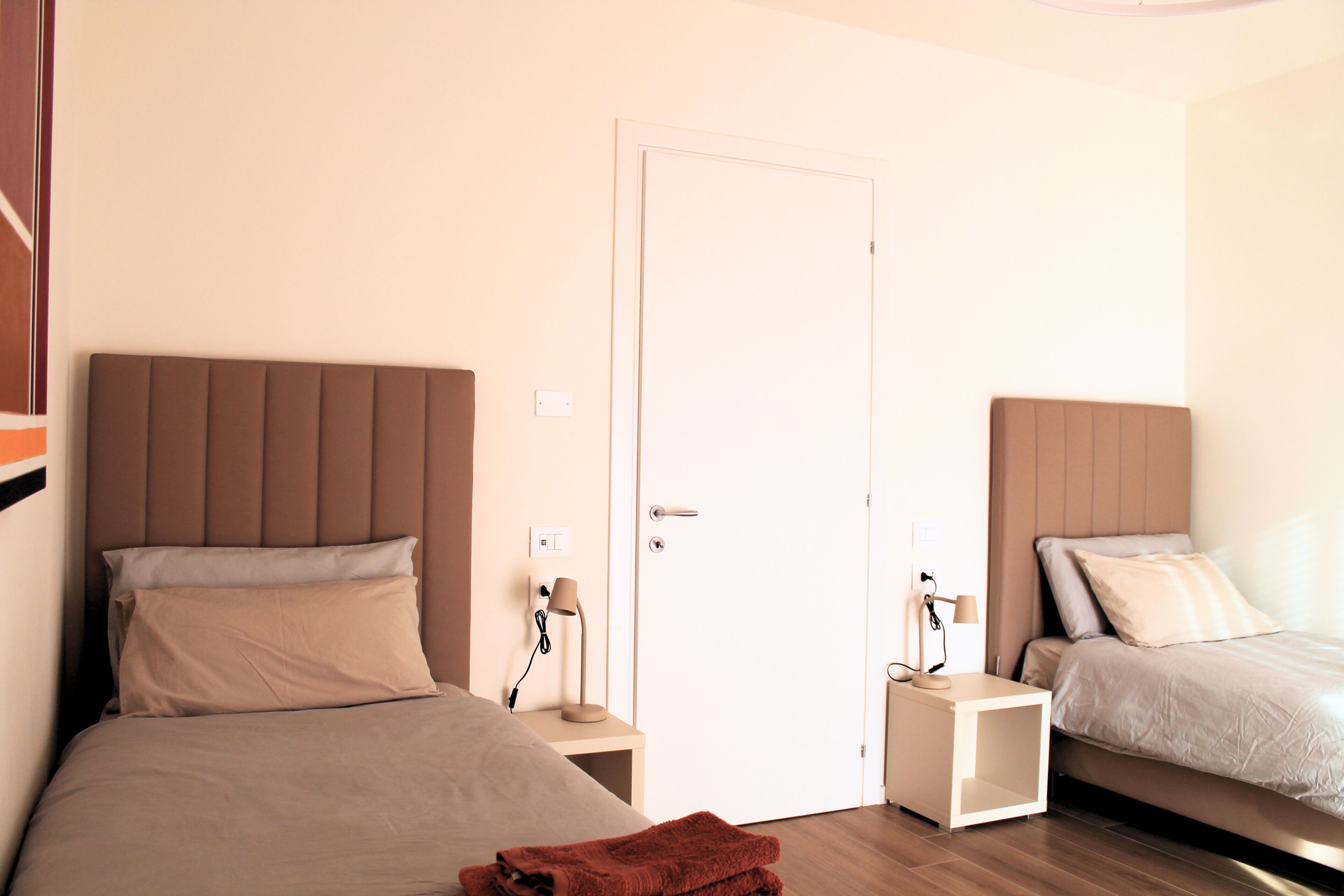 A bedroom with two beds, a door, bedside tables, and lamps.