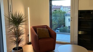 A modern living room with a sofa, a round table, a potted plant, and a view through a glass door. - Liverani (Imola)