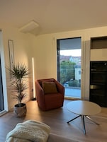 A modern living room with a sofa, a round table, a potted plant, and a view through a glass door.