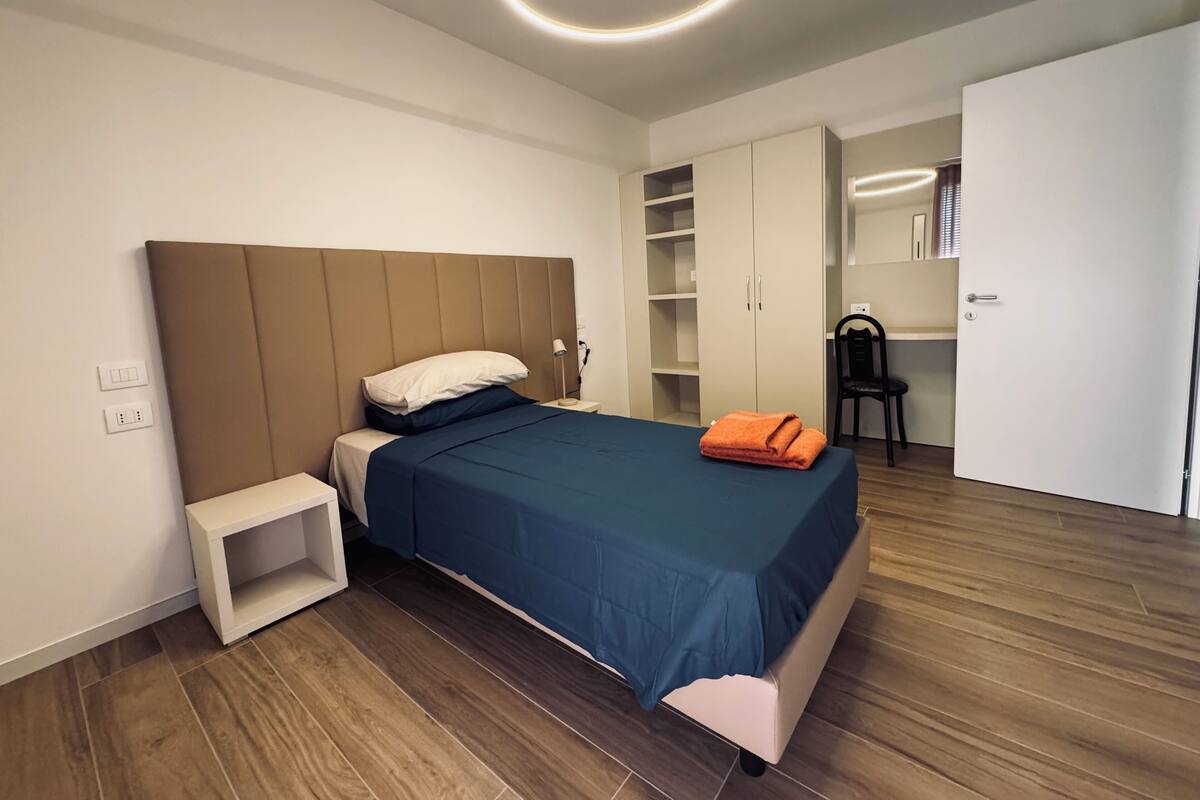 A modern bedroom with a bed, bedside table, wardrobe, and a desk area.
