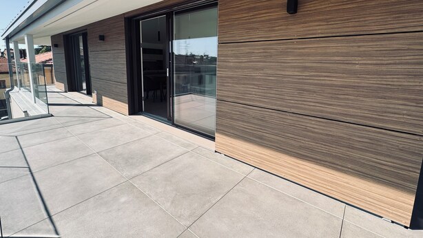 A modern building exterior with a glass door entrance, a covered outdoor seating area, and a tiled patio. - Liverani (Imola)