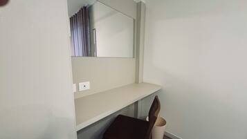 Una stanza piccola e pulita con una sedia di legno, uno scaffale bianco e uno specchio appeso al muro.
