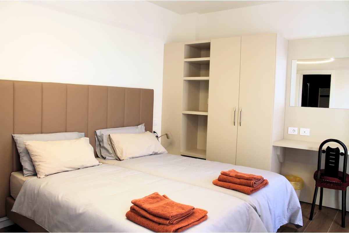 A hotel room with two beds, a wardrobe, a desk, and a chair.