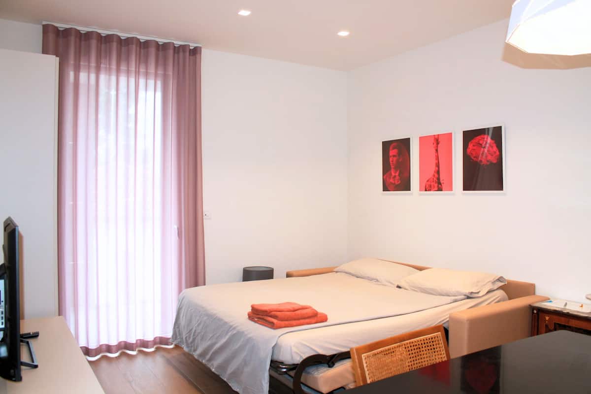 A hotel room with a bed, a desk, a chair, a television, and a window with curtains.