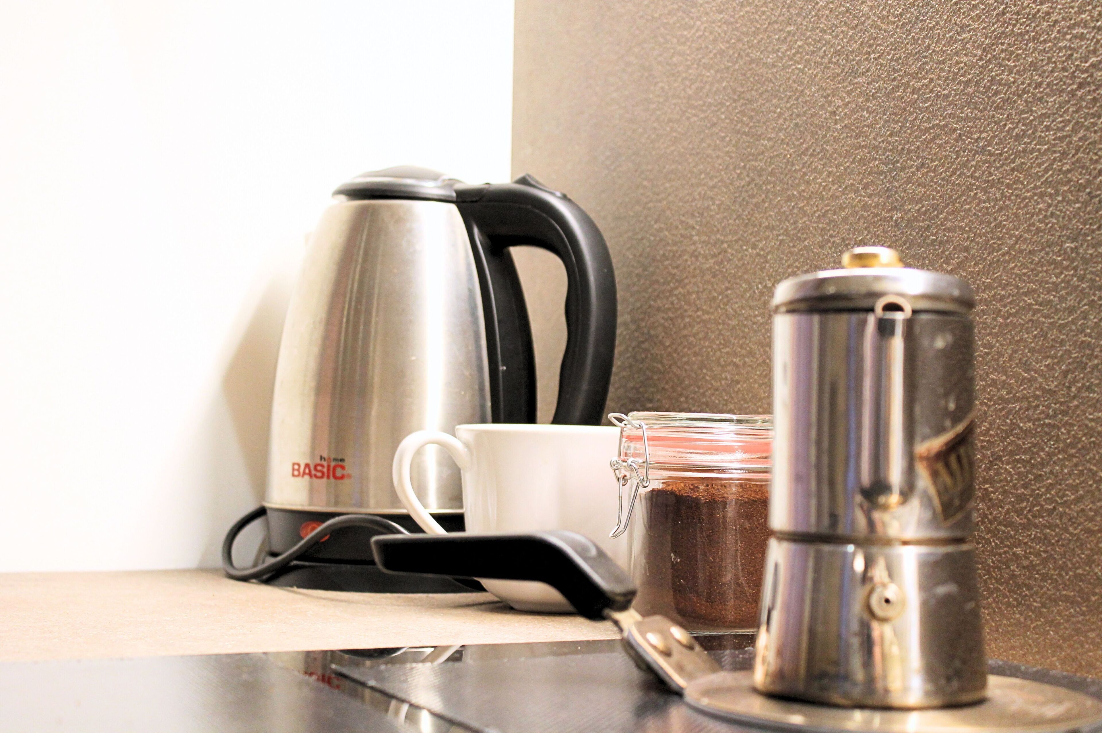A kitchen counter with a coffee maker, a white mug, and a stainless steel kettle.