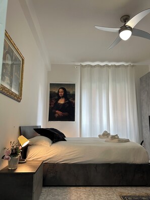 A bedroom with a bed, a ceiling fan, a painting of the Mona Lisa, a nightstand, and a window with curtains. - Candelor House | Apartment & Garden in Gianicolense (Roma)