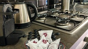 Een keuken met een gasfornuis, een koffiezetapparaat en een kom met koffiepads op het aanrecht.