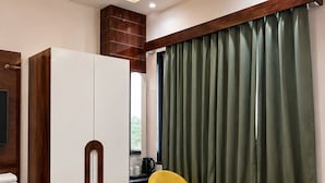 A modern room with a wardrobe, two yellow chairs, a green table, and a large window with curtains. - Dream House Club And Resort (Gonda)