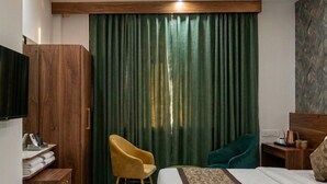 A hotel room with a bed, a desk, a chair, a television, and a ceiling fan. - Dream House Club And Resort (Gonda)
