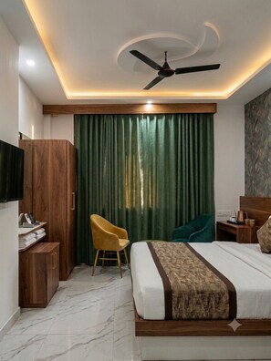 A hotel room with a bed, a desk, a chair, a television, and a ceiling fan. - Dream House Club And Resort (Gonda)