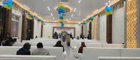 Un salón amplio con filas de sillas blancas, un escenario central con un letrero que dice 'BIENVENIDA, BEBÉ' y globos decorativos.