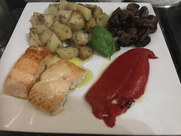 A plate with grilled chicken, roasted potatoes, mushrooms, and a basil leaf.