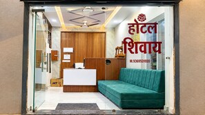 A hotel reception area with a reception desk, a green sofa, and a wooden panel wall. - Hotel Shivay - Near Mahakal Mandir (Ujjain)