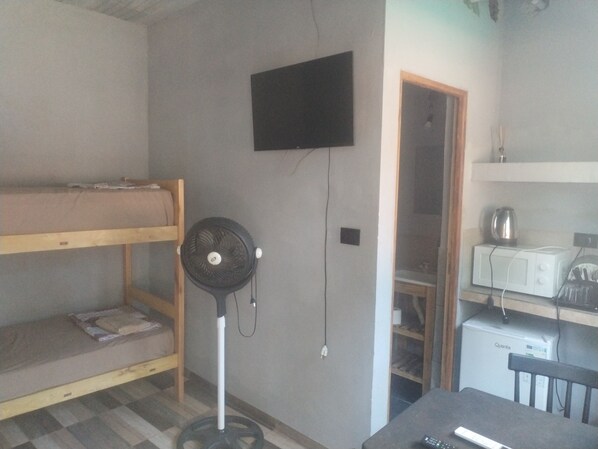 A room with a bunk bed, a standing fan, a microwave, and a television.