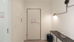 Un pasillo con una puerta blanca, una luz empotrada en la pared y una pequeña mesa con un vaso.