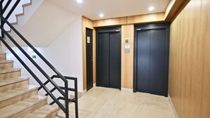 Un área de ascensor moderna con detalles de madera y una escalera con barandillas negras.
