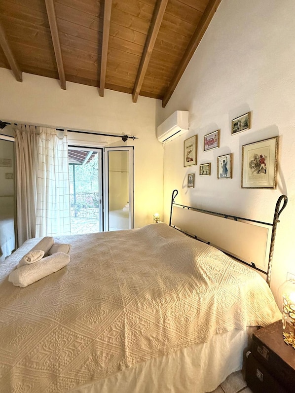 A bedroom with a bed, a window with curtains, a wall-mounted air conditioner, and several framed pictures.