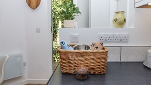 Eine Küche mit einem Korbwicker-Korb, der ein Glas, eine Schüssel und Hausschuhe enthält, einer Topfpflanze und einer herzförmigen Holzdekoration an der Wand.