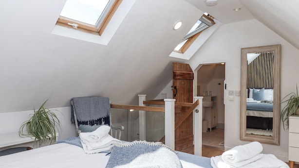 Ein Schlafzimmer mit Oberlicht, einer Holztreppe, einem großen Spiegel und Blick ins Badezimmer.