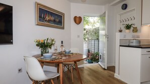 Ein Essbereich mit einem Holztisch, weißen Stühlen und einem Gemälde mit Segelbooten. Eine herzförmige Dekoration hängt an der Wand, und über der Tür ist eine Uhr zu sehen.