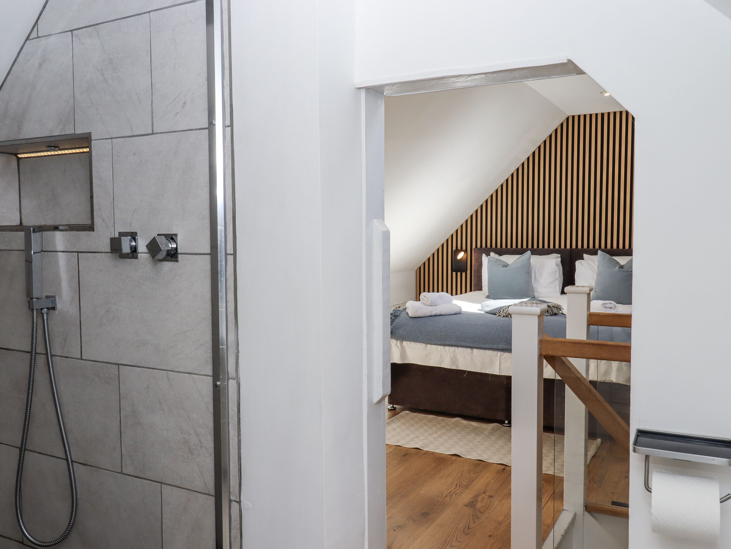 A modern bathroom with a shower and a bedroom with a bed, a nightstand, and a wooden headboard.