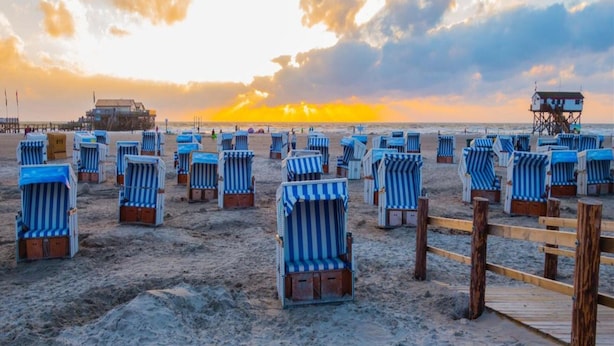 Una playa con hileras de sillas de playa a rayas y un camino de madera.