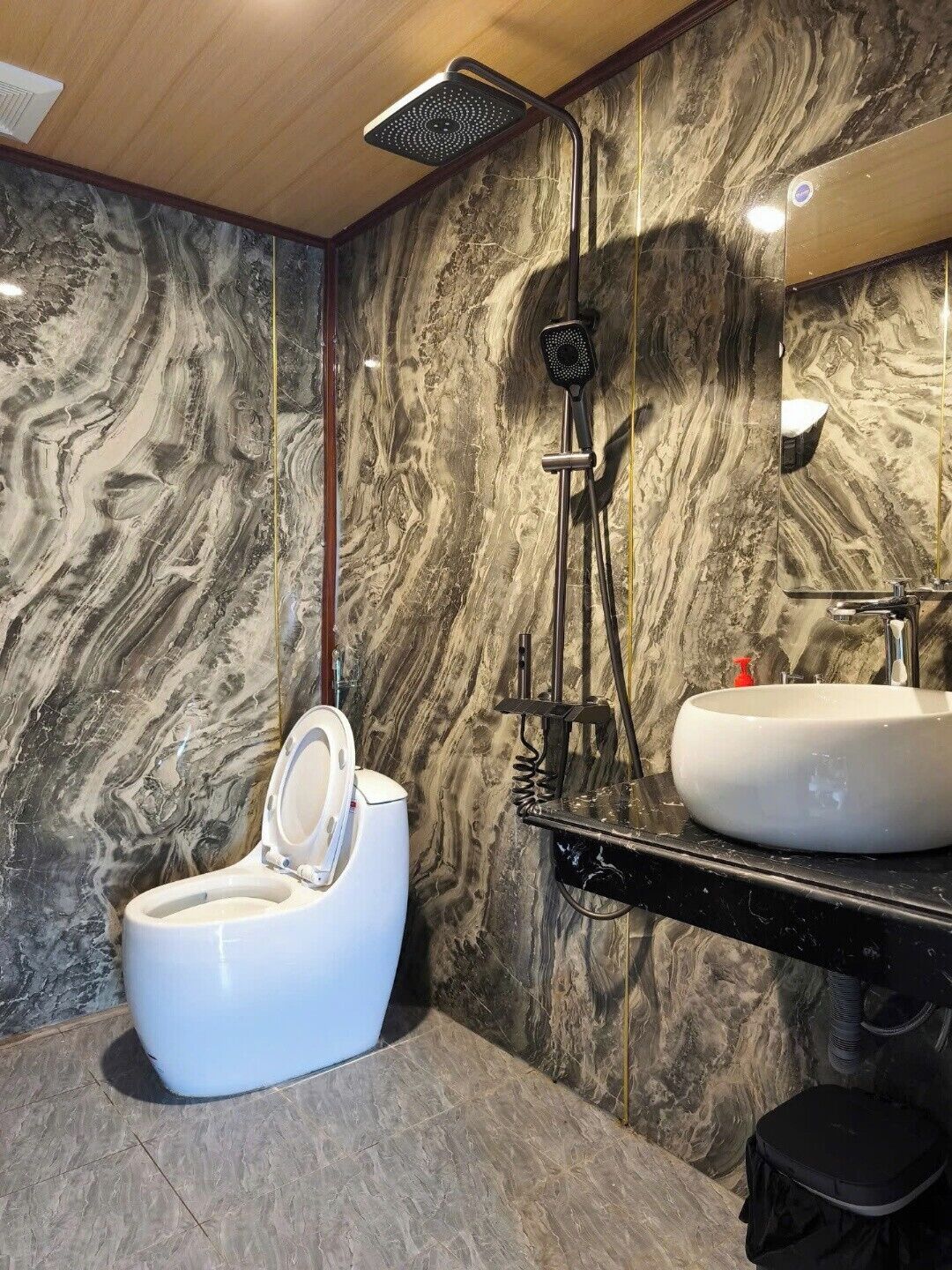 A modern bathroom with a marble wall, a white toilet, a black sink, and a shower.