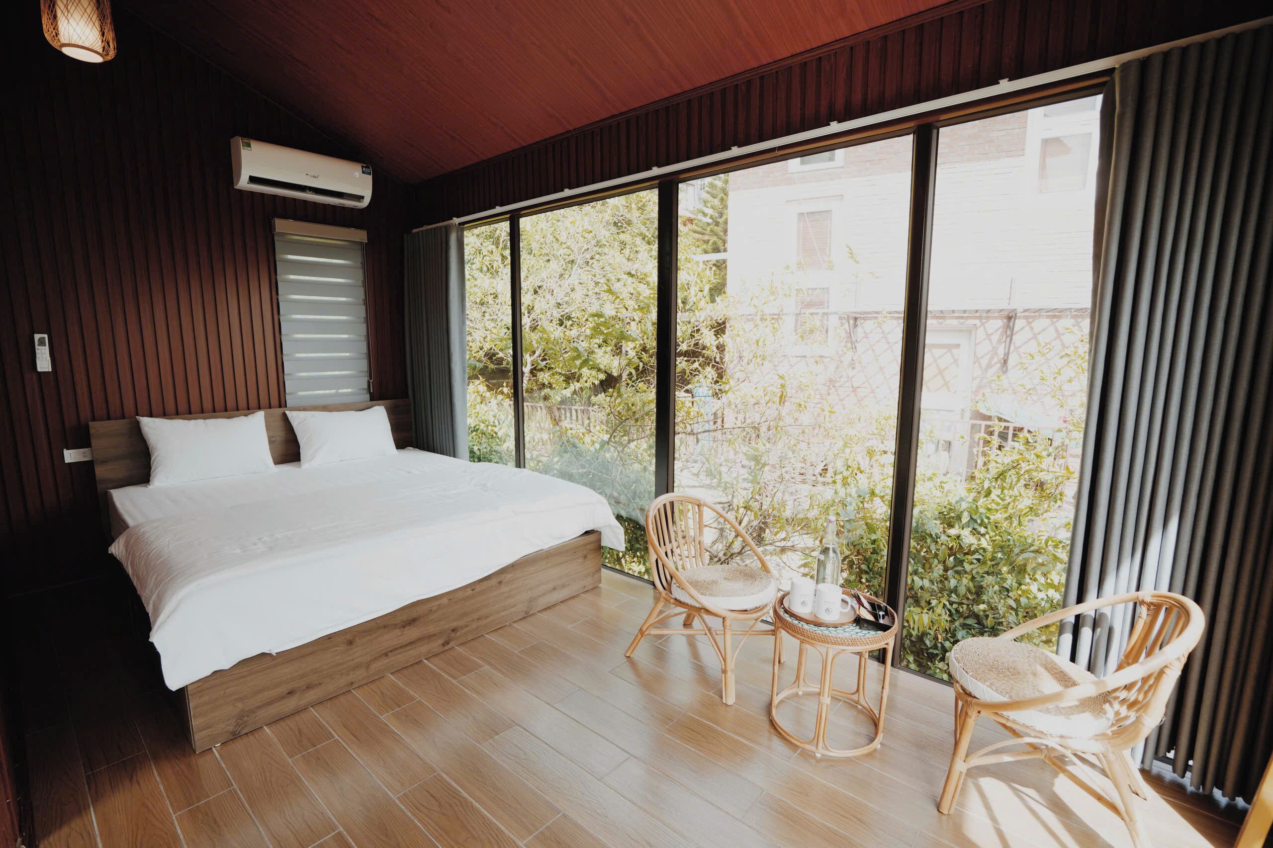 Une chambre avec un grand lit, un plancher en bois et une vue dégagée sur l’extérieur grâce à de grandes fenêtres.