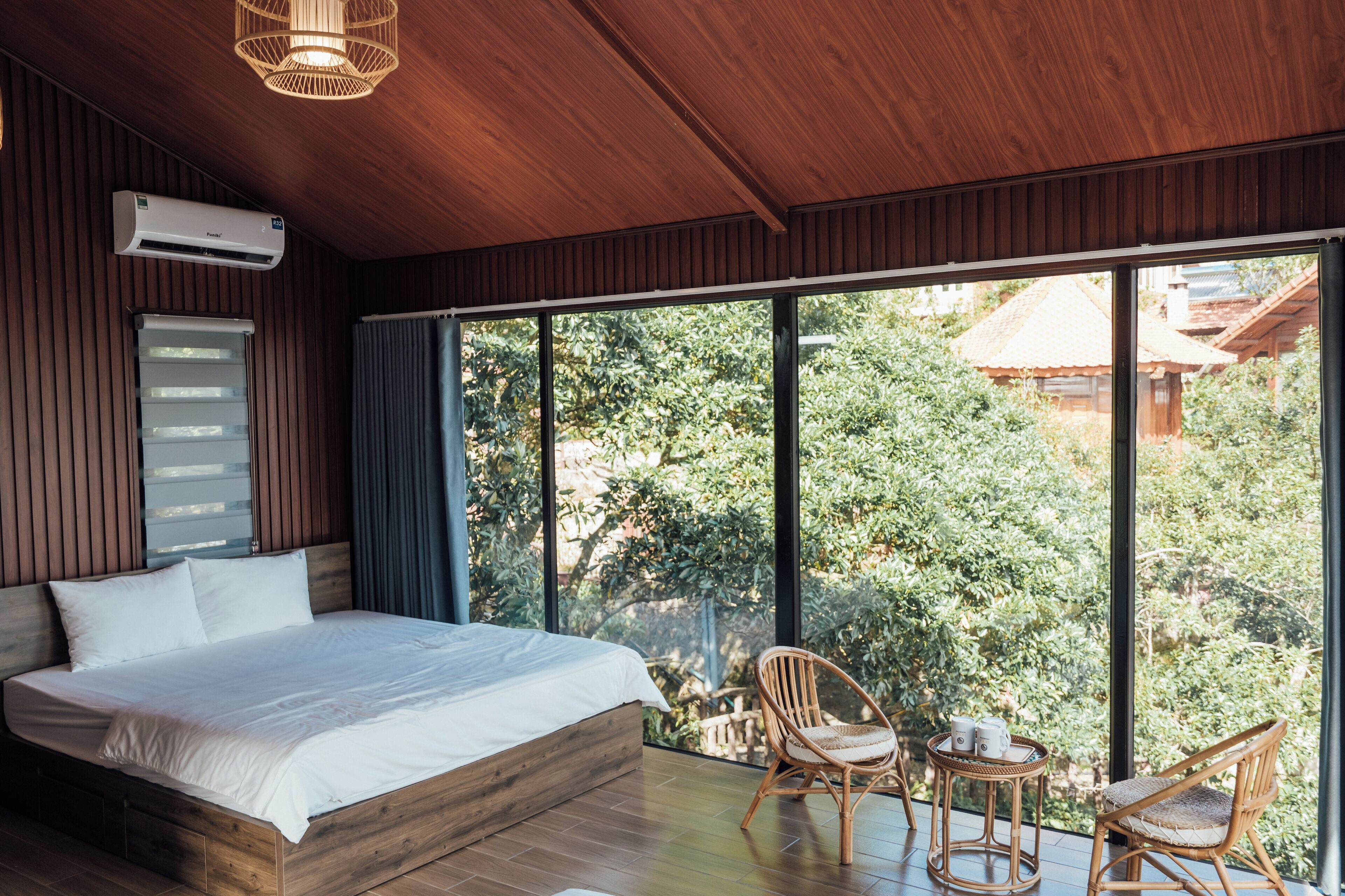 A bedroom with a large bed, wooden walls, and a view of greenery outside.