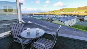 Ein Balkon mit Tisch und Stühlen, mit Blick auf einen Caravanpark mit mehreren Wohnwagen und einer hügeligen Landschaft im Hintergrund.