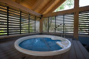 Un bain à remous situé dans un espace extérieur abrité, doté d’une terrasse en bois et de stores métalliques.