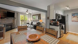 Una cocina moderna con horno empotrado, microondas y refrigerador. Hay una zona de comedor con una mesa y sillas de madera, y una chimenea.