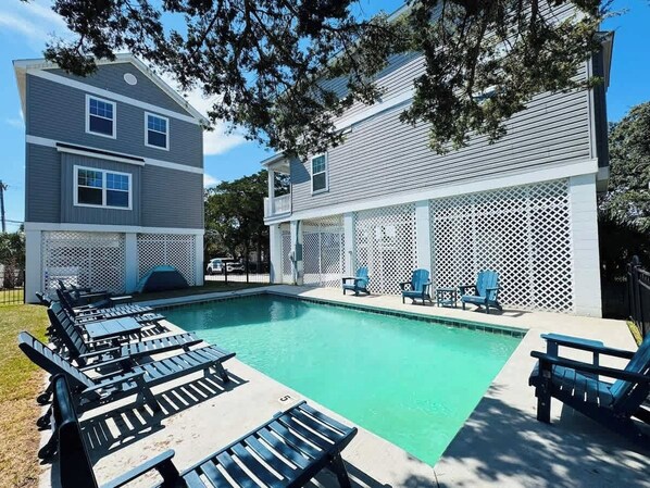 A swimming pool with lounge chairs and a covered area with a lattice fence.