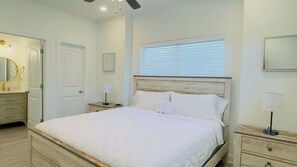 A bedroom with a large bed, a nightstand, a dresser, a mirror, and a ceiling fan.