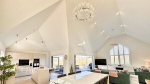 Un ampio appartamento in stile loft con soffitto alto, cucina con isola centrale, zona pranzo, soggiorno con divano verde e ampie finestre che offrono luce naturale.